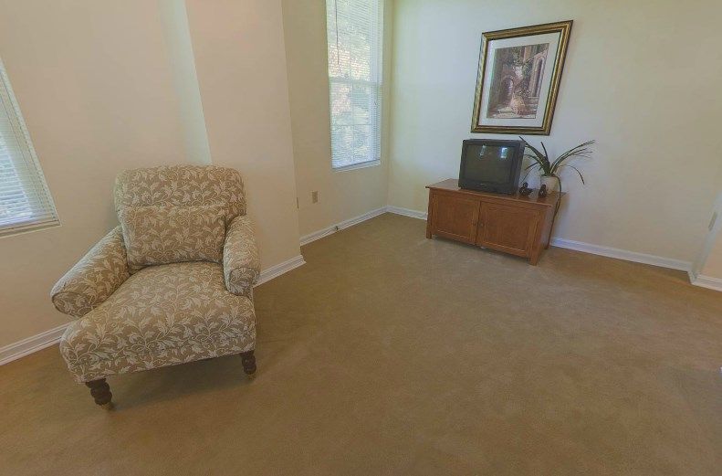 A cozy living room with a patterned chair, a TV on a wooden stand, and a decorative painting.