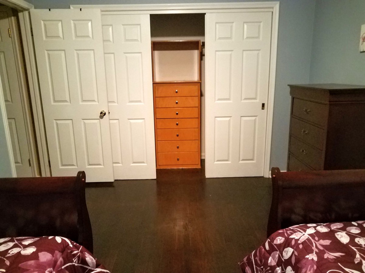 A bedroom with an open closet revealing a wooden dresser inside.