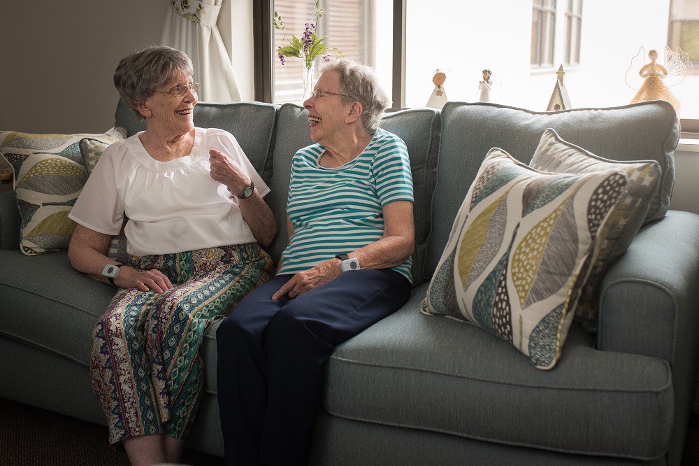 Two elderly women sitting on a sofa, engaged in a friendly conversation.