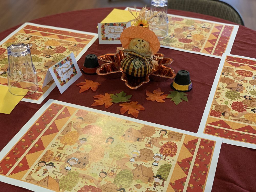 A festive Thanksgiving table setting with autumn-themed placemats and a pumpkin centerpiece.