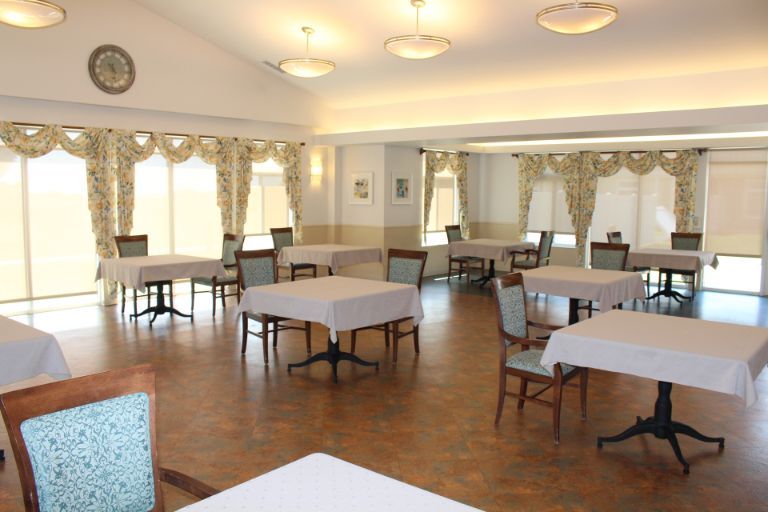 An empty dining room with neatly arranged tables and chairs, decorated with curtains and lit by overhead lights.