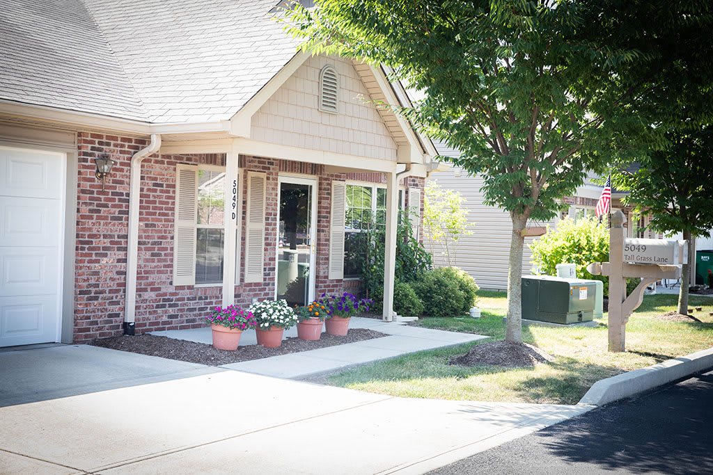 A cozy house with a brick exterior and a front porch, surrounded by plants and trees.