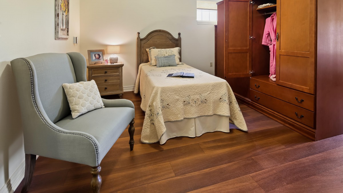 A cozy bedroom with a single bed and wooden flooring, featuring a nightstand and an armchair.