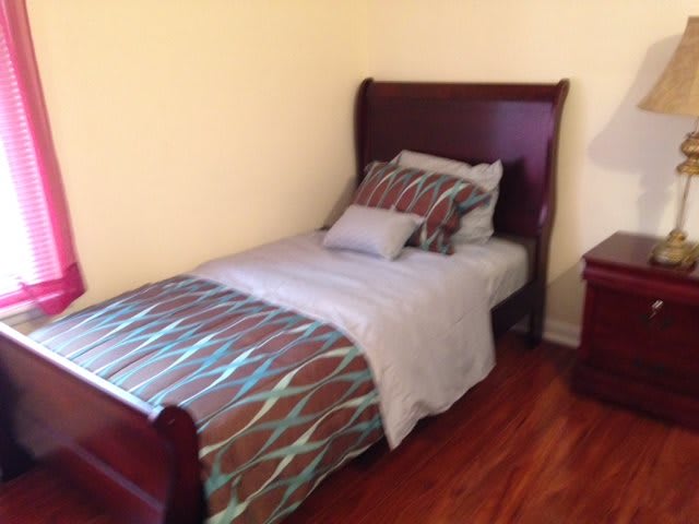 A simple bedroom setup featuring a single bed with patterned bedding, a wooden floor, and a nightstand.