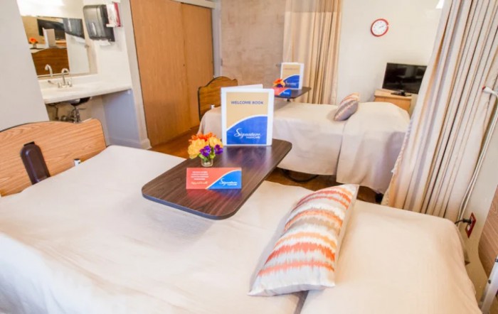 A cozy hotel room featuring twin beds with a side table, decorated with pillows and equipped with a television.