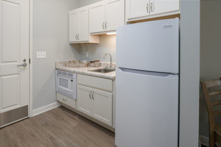 A compact kitchen with white cabinets, a refrigerator, microwave, and a sink.