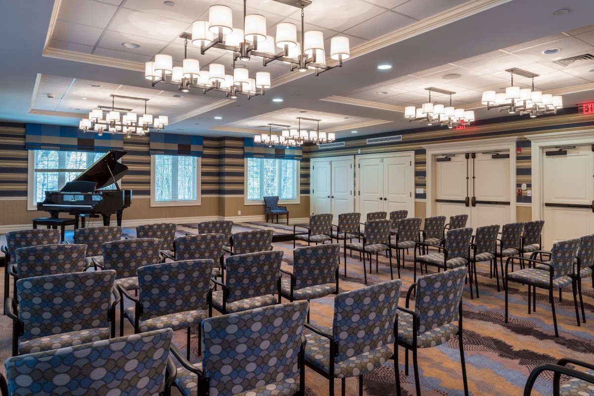 A well-lit conference room with rows of patterned chairs and a grand piano.