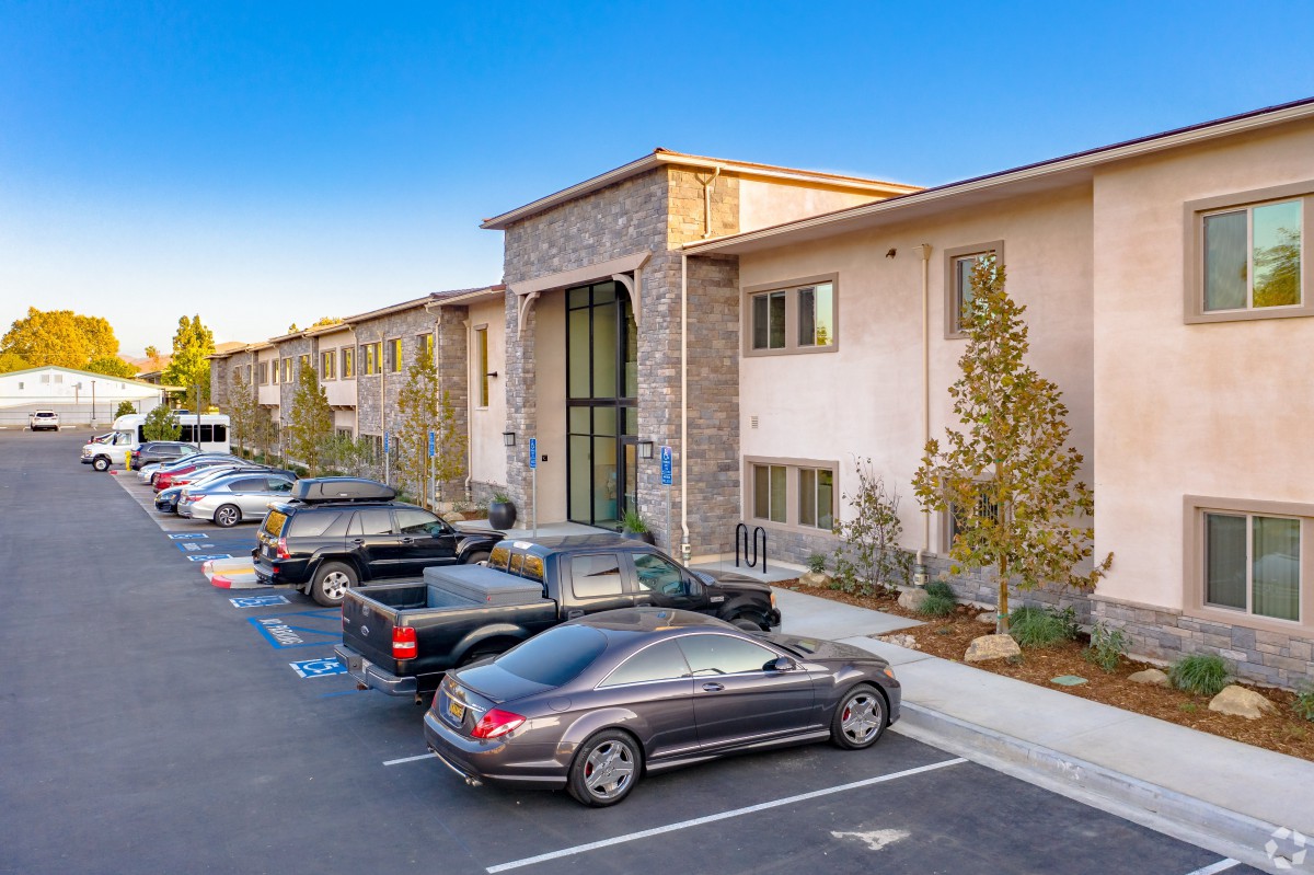 A modern apartment building with a parking lot filled with cars.