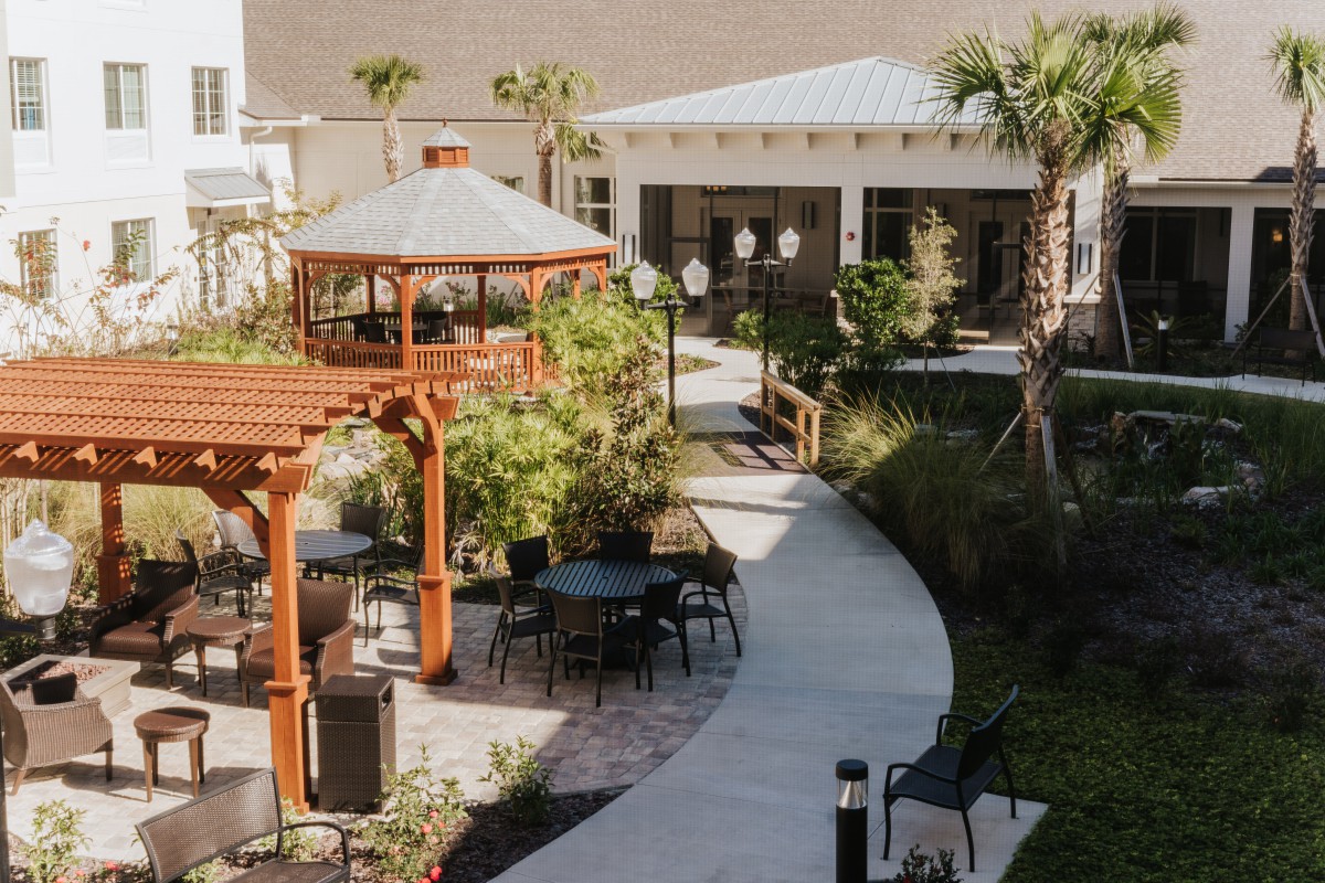 A tranquil outdoor garden featuring a gazebo, pathway, and seating areas surrounded by lush greenery.