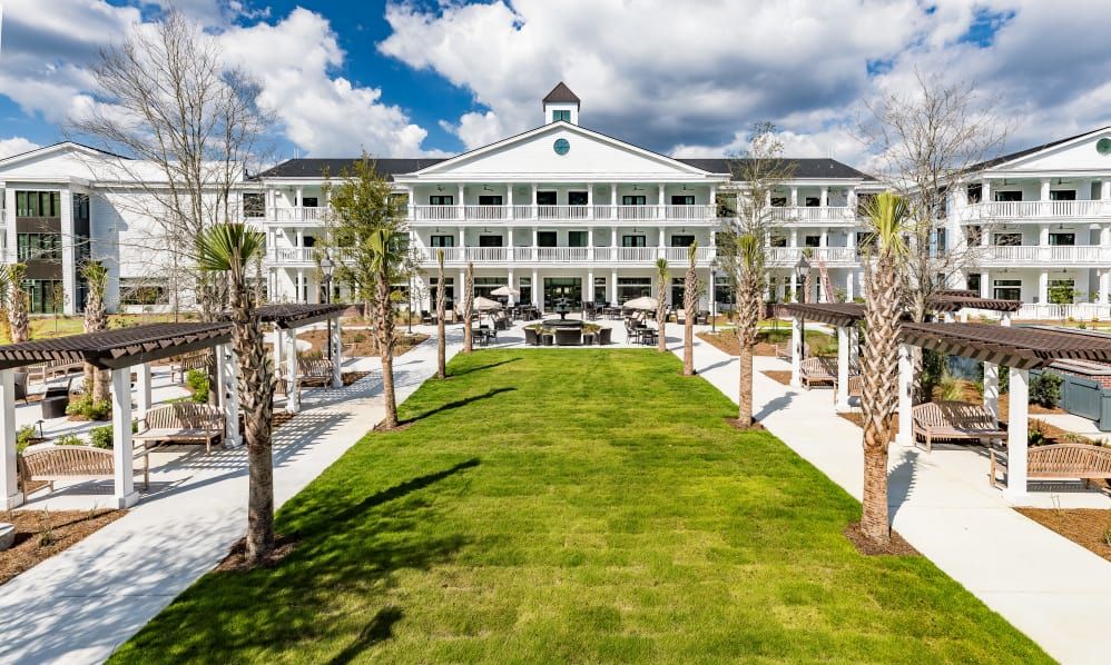 A picturesque view of a grand hotel with a manicured lawn and palm trees under a partly cloudy sky.