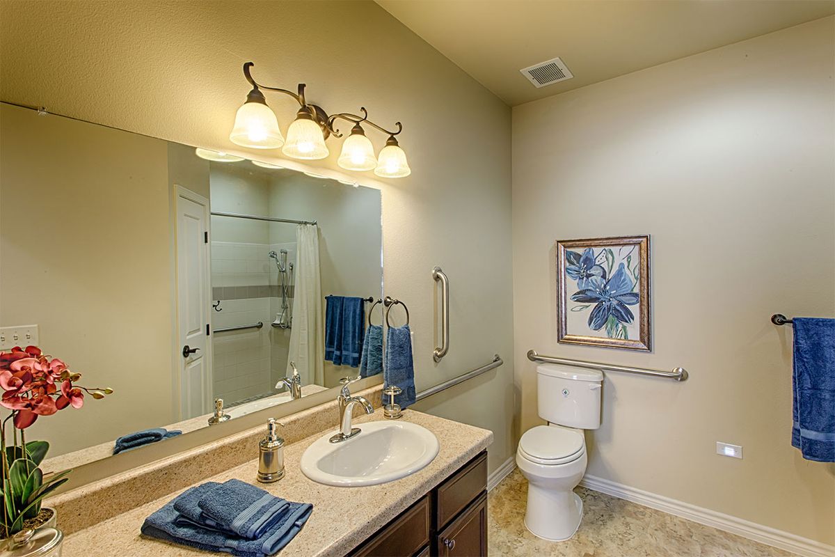 A clean and well-lit bathroom featuring a sink, mirror, toilet, and shower.