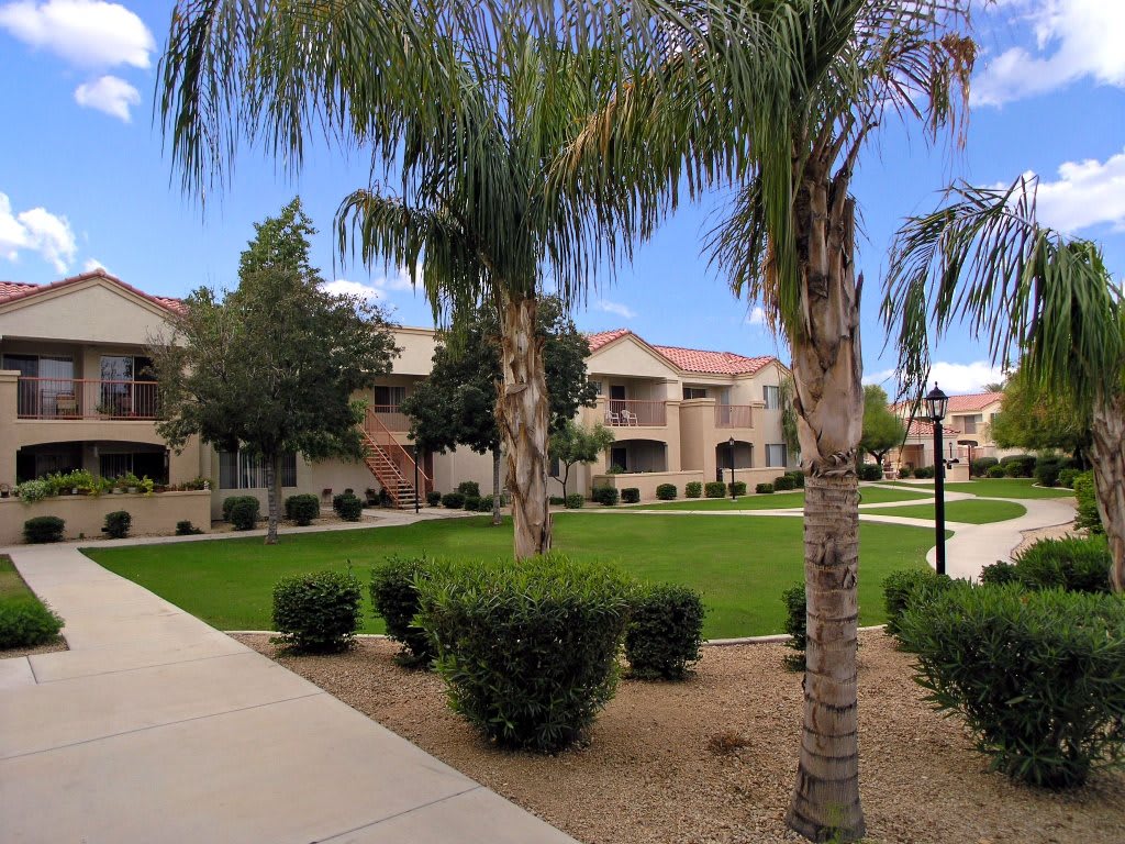 A well-maintained apartment complex with palm trees and a green lawn.
