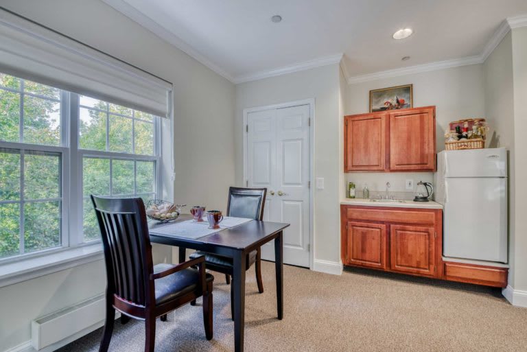A cozy dining area featuring a dark wooden table with chairs, a window letting in natural light, and wooden cabinets.