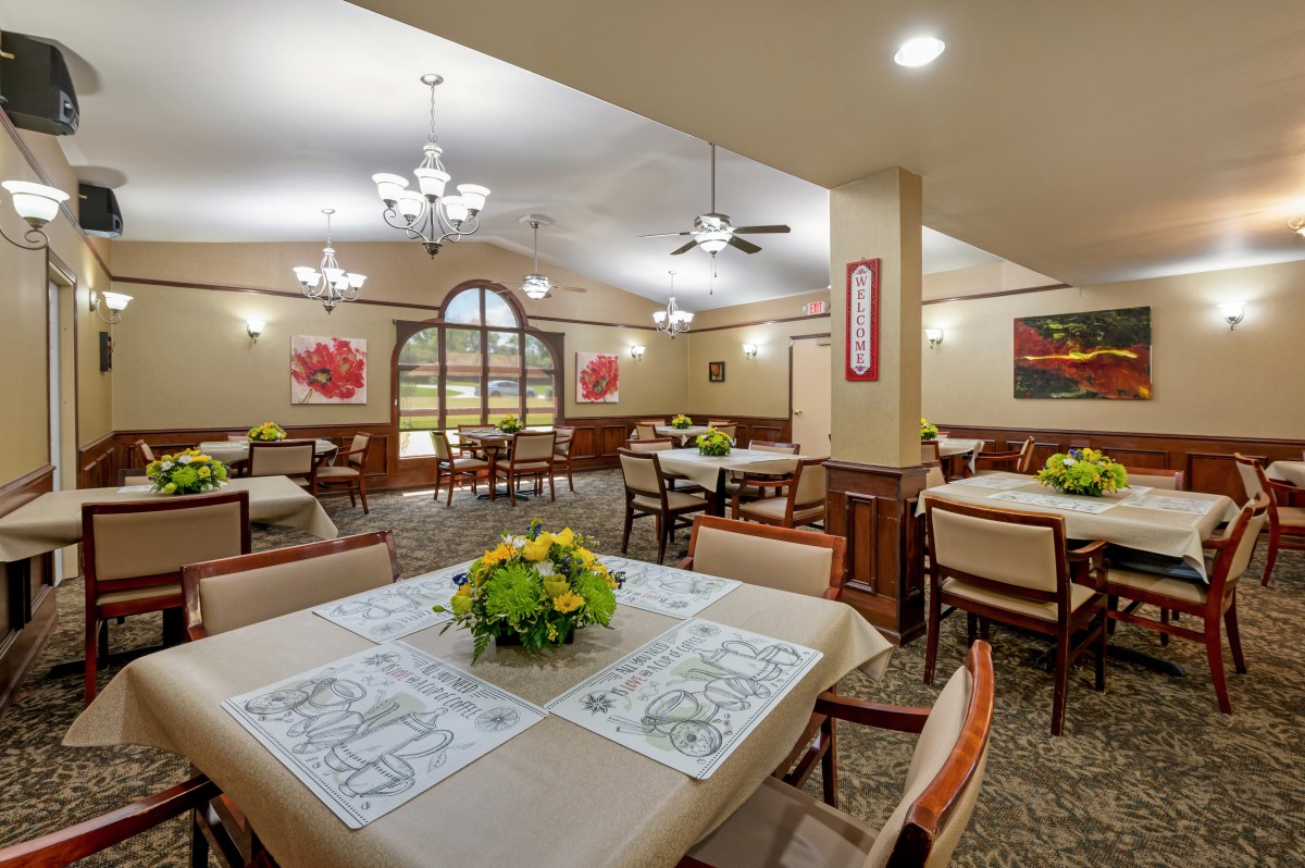 A well-appointed dining room featuring multiple tables with decorative centerpieces, comfortable chairs, and elegant lighting fixtures.