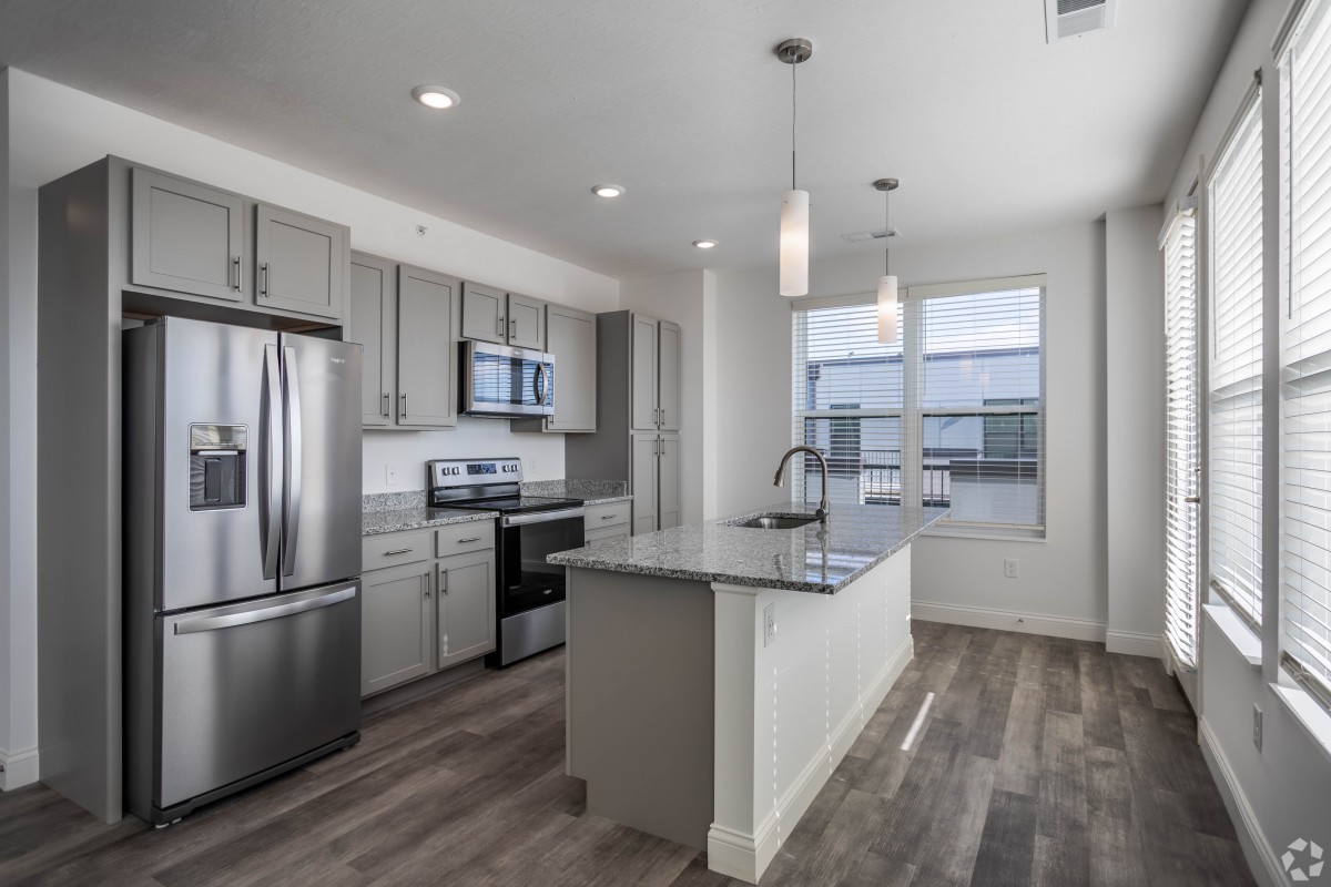 A modern kitchen with stainless steel appliances, featuring a central island and pendant lighting in an open floor plan setting.