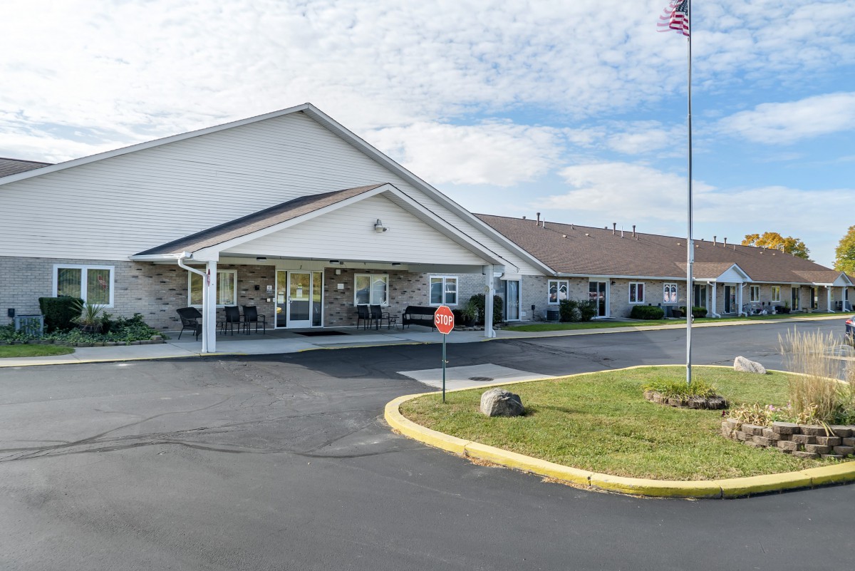 A single-story building with a landscaped front and an American flag on a pole under a partly cloudy sky.