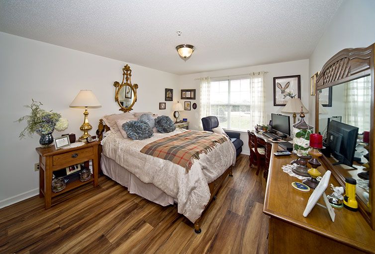 A cozy bedroom featuring a large bed, wooden flooring, and a computer desk near the window.