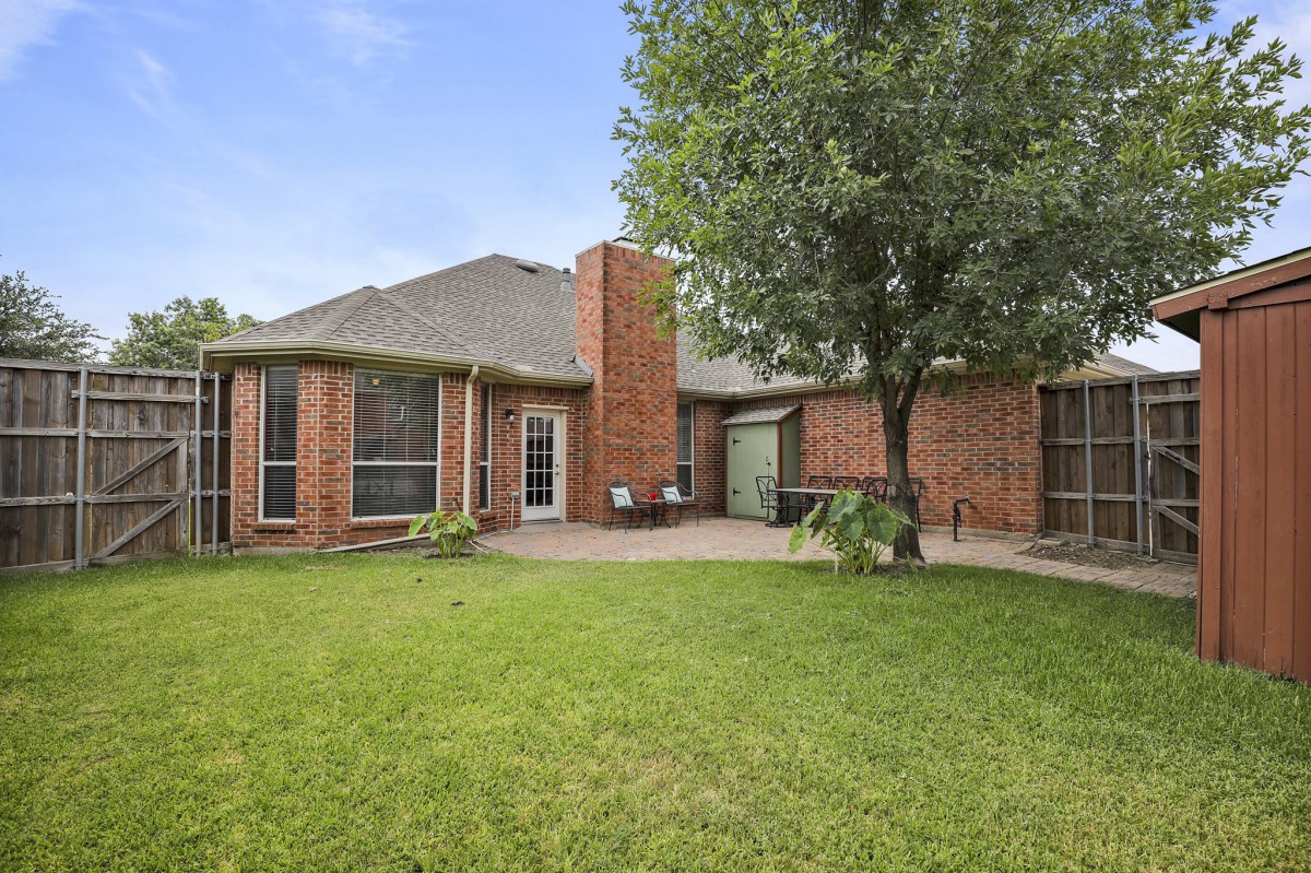 A spacious backyard with a brick house, well-maintained lawn, and a patio area.