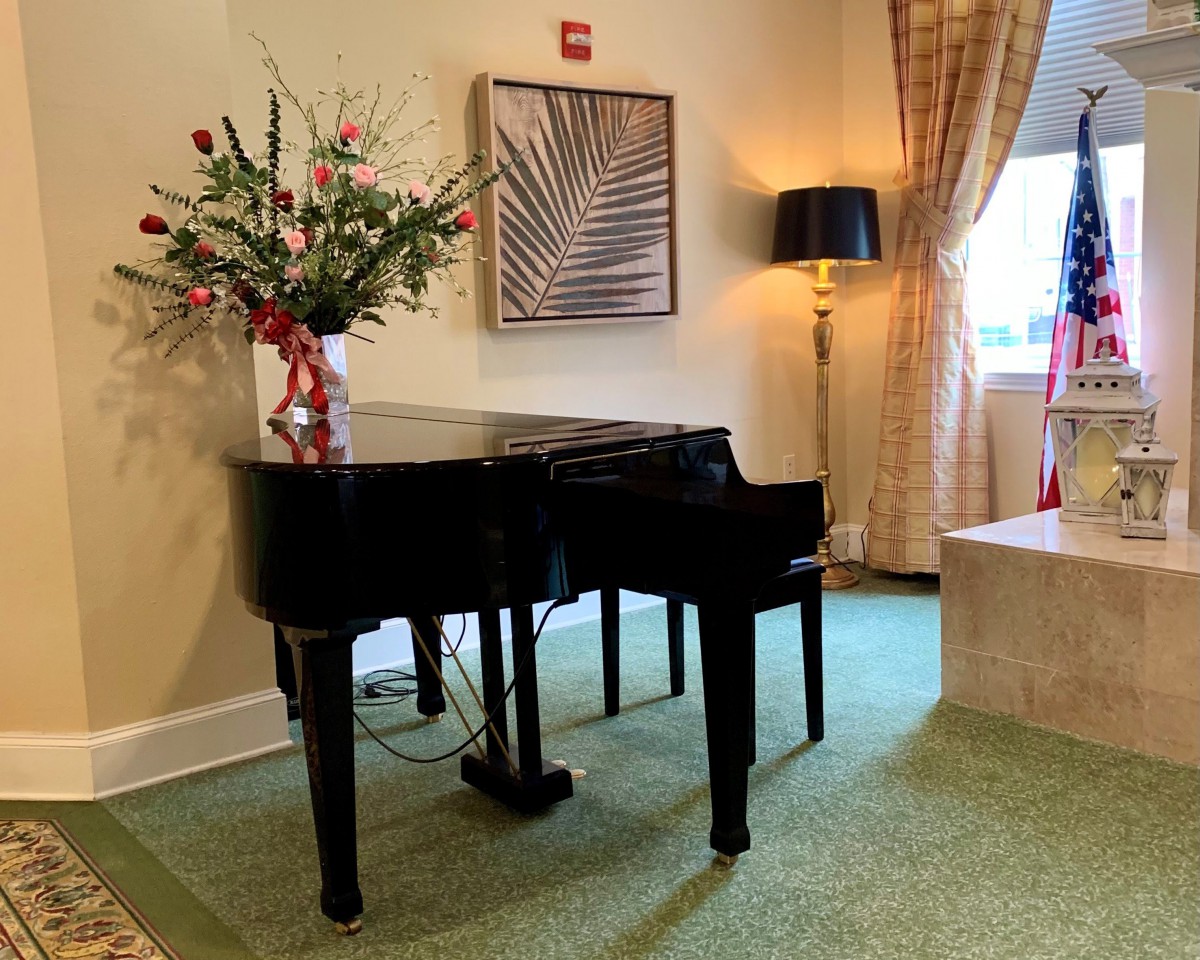 A grand piano elegantly placed next to a vase of flowers and a stylish lamp in a well-decorated room with artwork on the wall.