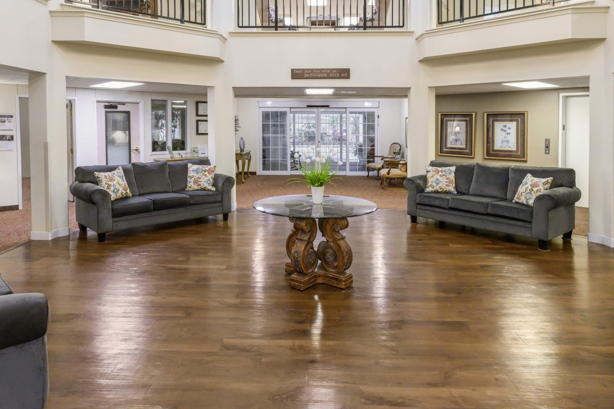 A spacious lobby area with wooden flooring, featuring sofas and a central table.