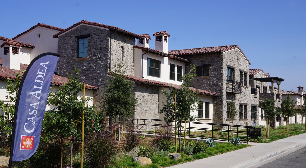 A modern stone residential building with lush landscaping under a clear blue sky.