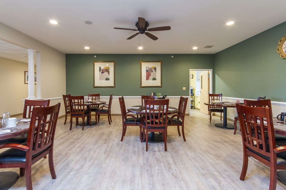 A dining room with several tables and chairs, featuring wood flooring, wall art, and a ceiling fan.