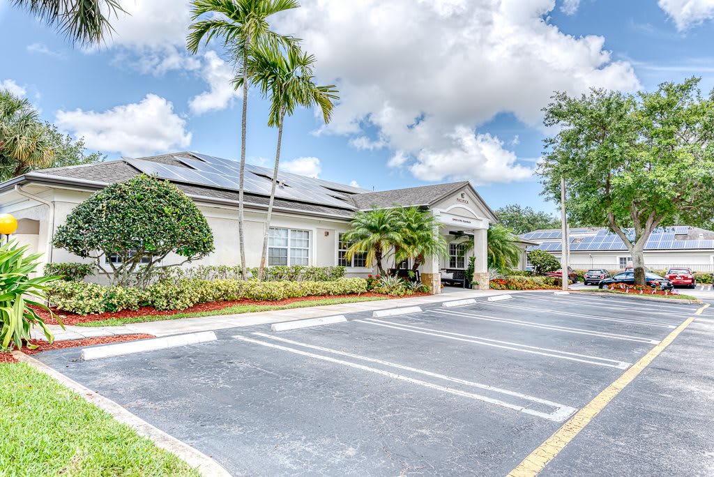 A tropical building with solar panels and a parking lot under a cloudy sky.