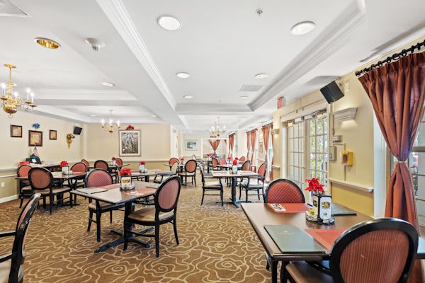 A spacious and elegantly decorated dining room with multiple tables and chairs, featuring large windows and ambient lighting.