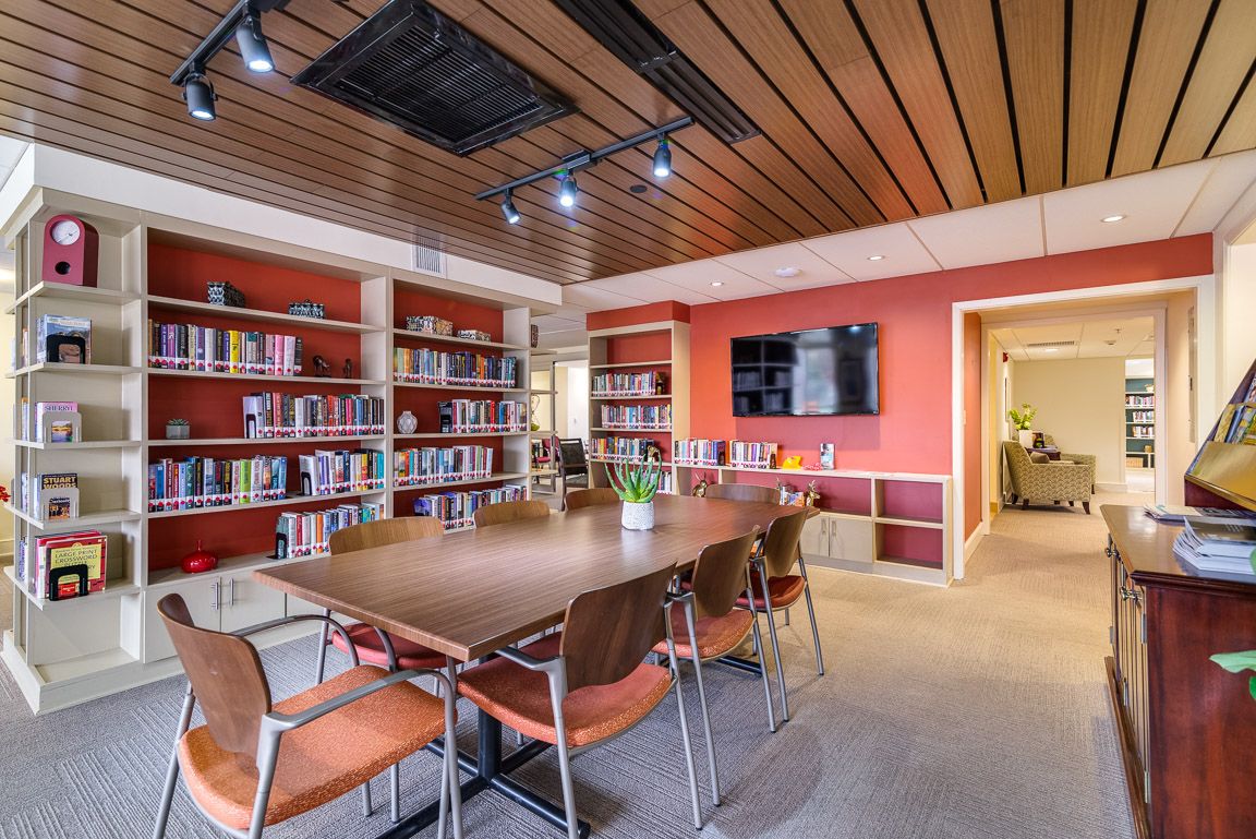 A modern conference room with a large meeting table surrounded by chairs, bookshelves lining the walls, and a television mounted on the wall.