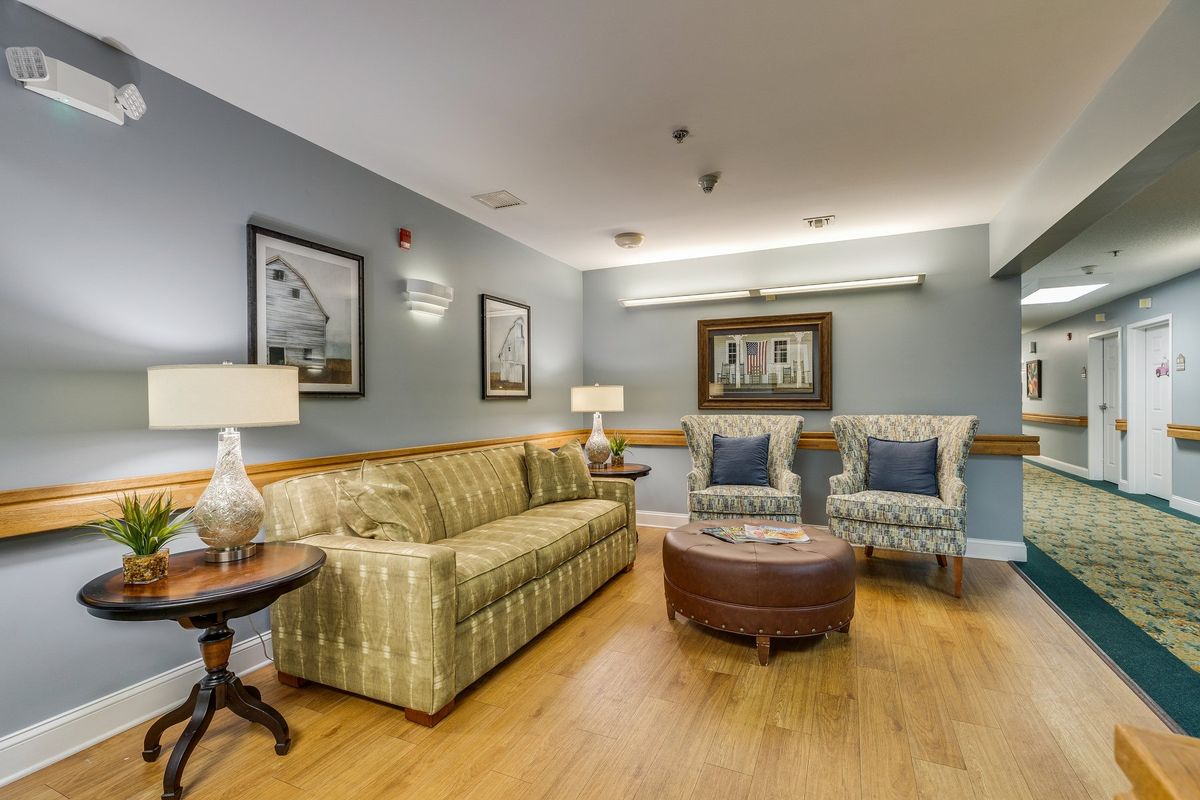 A cozy living room with a sofa, two chairs, a coffee table, and decorative elements like lamps and framed pictures on the walls.