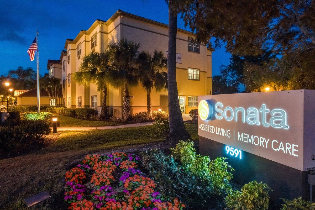 A nighttime view of a building with illuminated signage and landscaped surroundings.