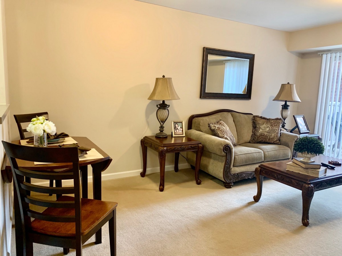 A cozy living room with a sofa, coffee table, side tables with lamps, and a dining area.