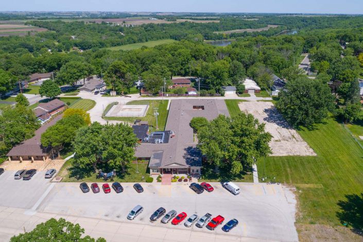 Aerial view of a building surrounded by trees with a parking lot and several cars in front.