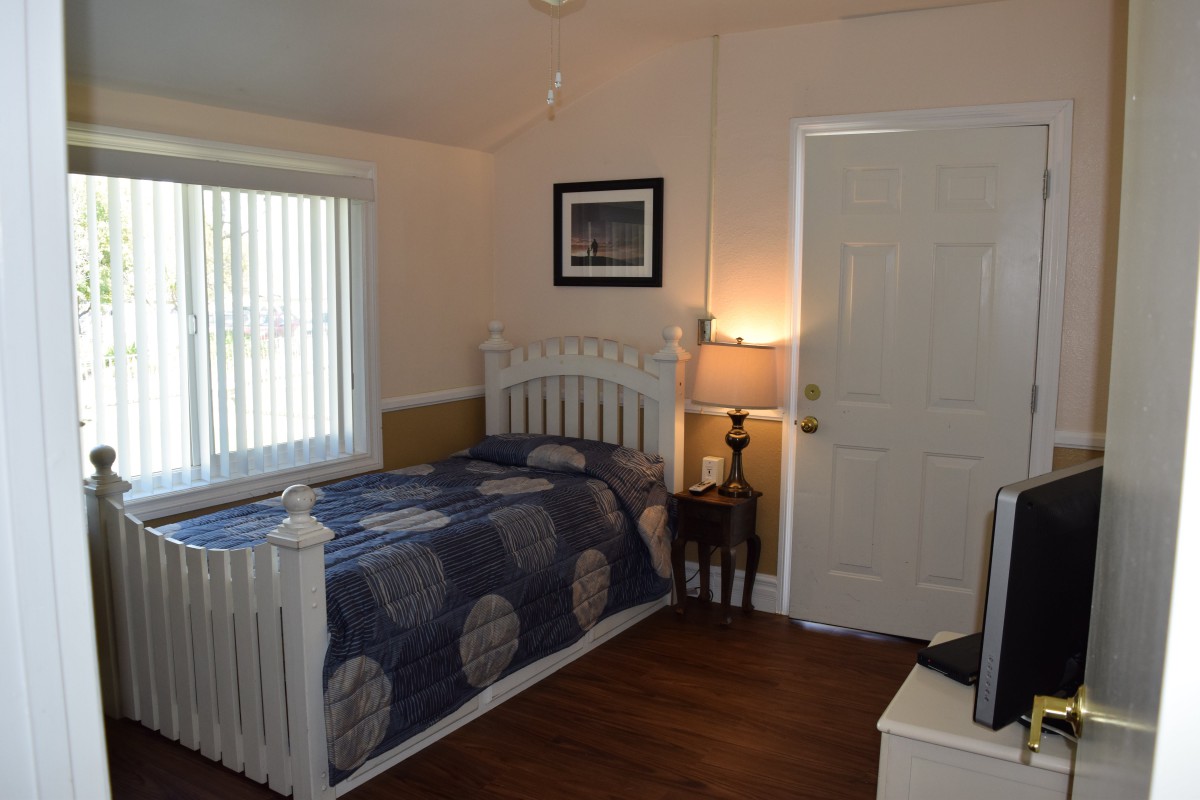 A cozy bedroom with a single bed, lamp, and a window letting in natural light.