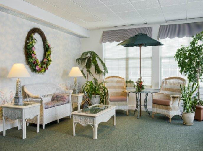 A cozy living room with white furniture, decorative plants, and a wreath on the wall.
