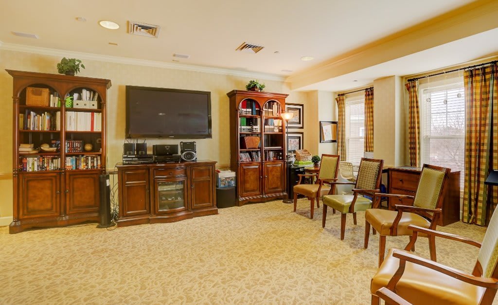 A cozy living room with wooden furniture, a large television, and several chairs arranged neatly.