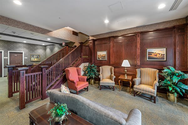 A cozy living room with comfortable armchairs and elegant wood paneling, featuring a staircase in the background.