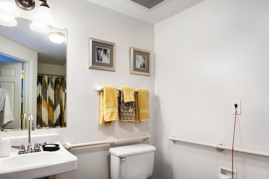 A neatly organized bathroom with yellow towels, framed pictures on the wall, and a modern sink area.