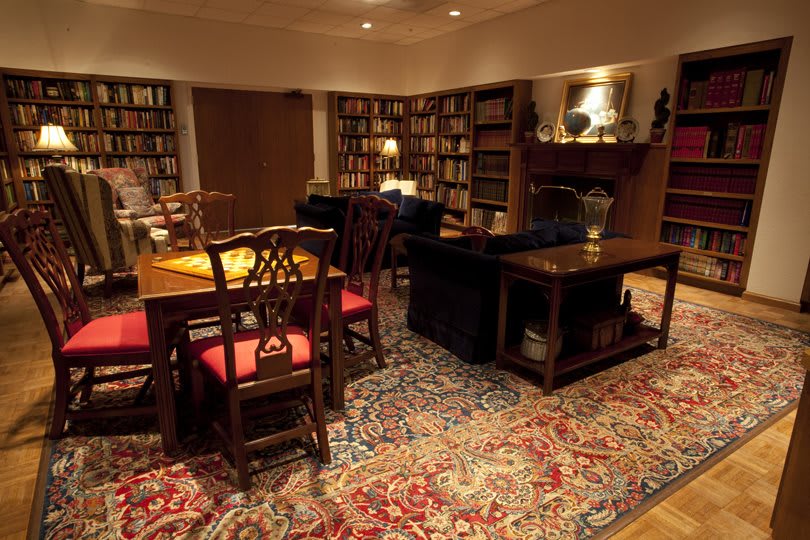 A cozy library room with bookshelves, a table with chairs, and a patterned carpet.