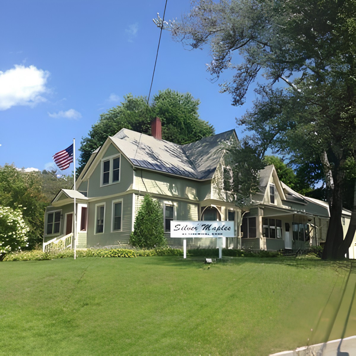A large house with an American flag and a sign on a sunny day.