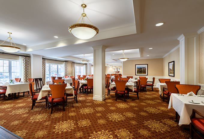 A spacious dining room with neatly arranged tables and chairs, featuring elegant lighting and decor.