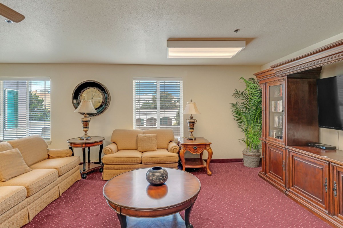 A cozy living room with a sofa, chairs, and a central coffee table, decorated with lamps and an indoor plant.