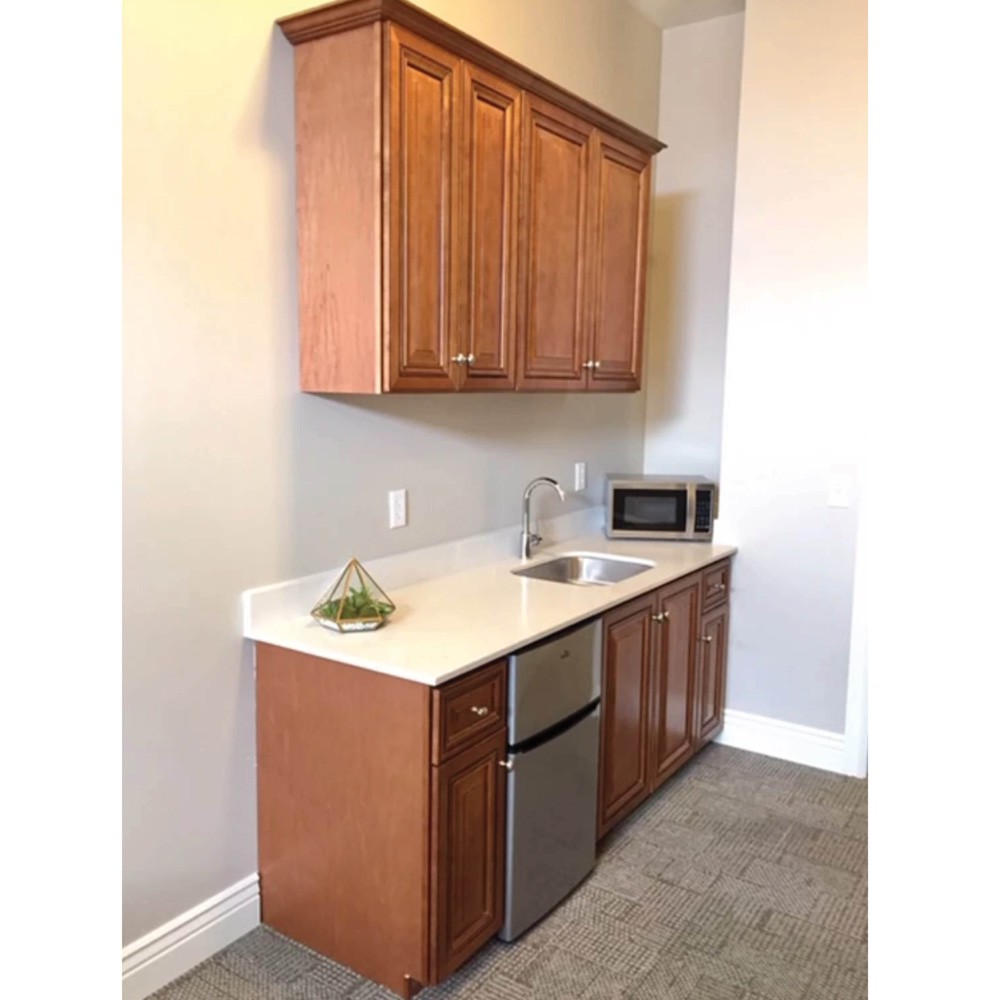 A compact kitchen area featuring wooden cabinets, a countertop with a sink, a microwave, and a mini fridge.