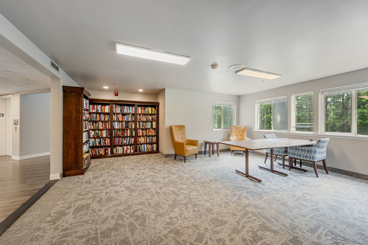 A cozy reading area with bookshelves, comfortable chairs, and natural light from large windows.