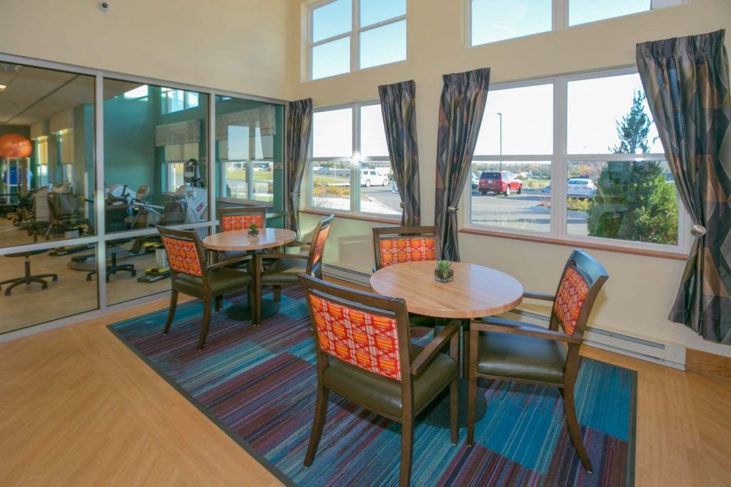 A cozy dining area with tables, chairs, and large windows letting in natural light.