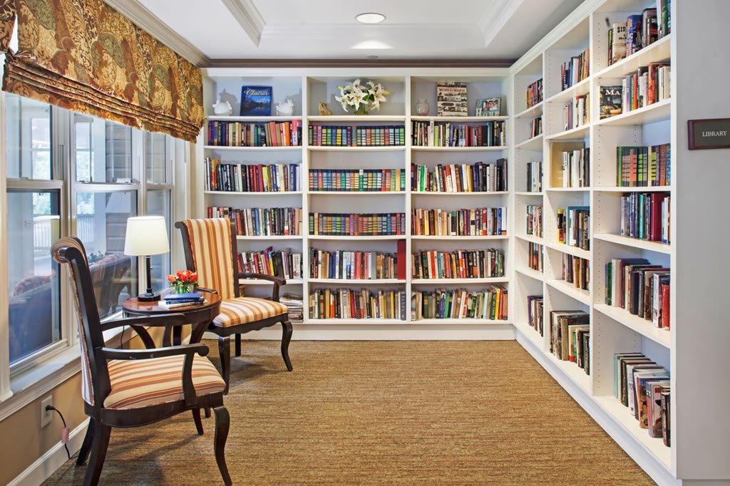 A cozy library with white bookshelves filled with books and comfortable armchairs.