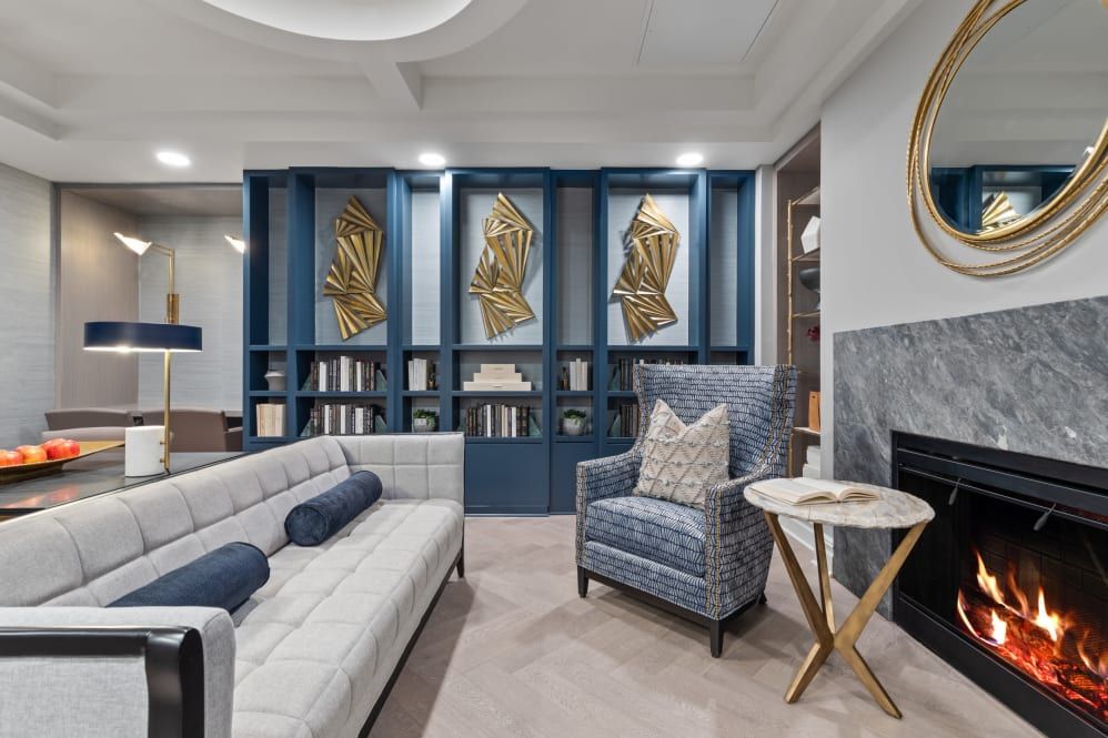 A modern living room with a blue and white color scheme, featuring abstract gold wall art, a cozy couch, an armchair, and a stylish bookshelf.