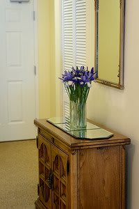 A hallway featuring a wooden cabinet with a glass vase of purple flowers and a mirror above.