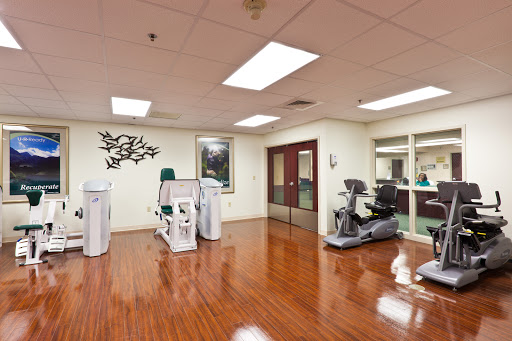 A well-equipped physical therapy room featuring various exercise machines and a polished wooden floor.