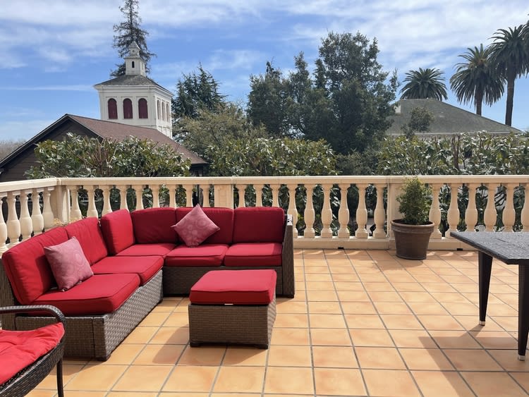 A sunny terrace with red-cushioned patio furniture and potted plants.